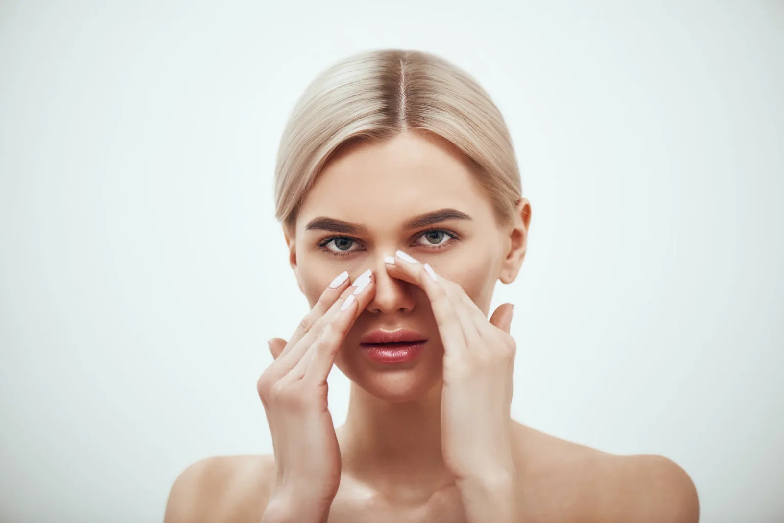 Woman examining her nose with both hands against a neutral background